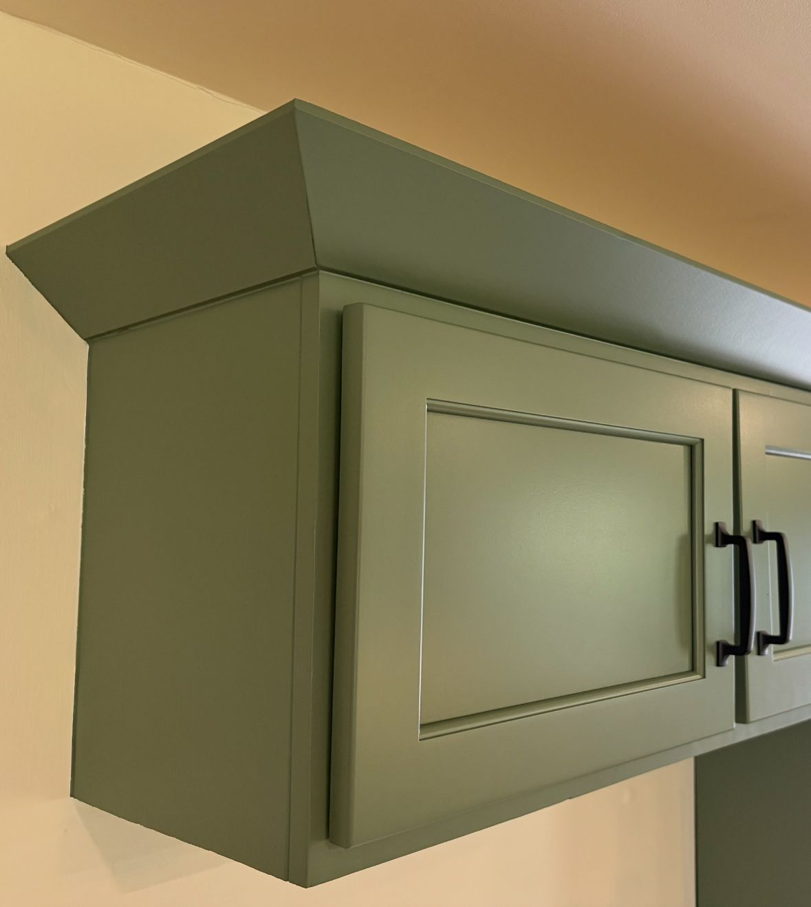 Green kitchen cabinet with crown molding and black handles.