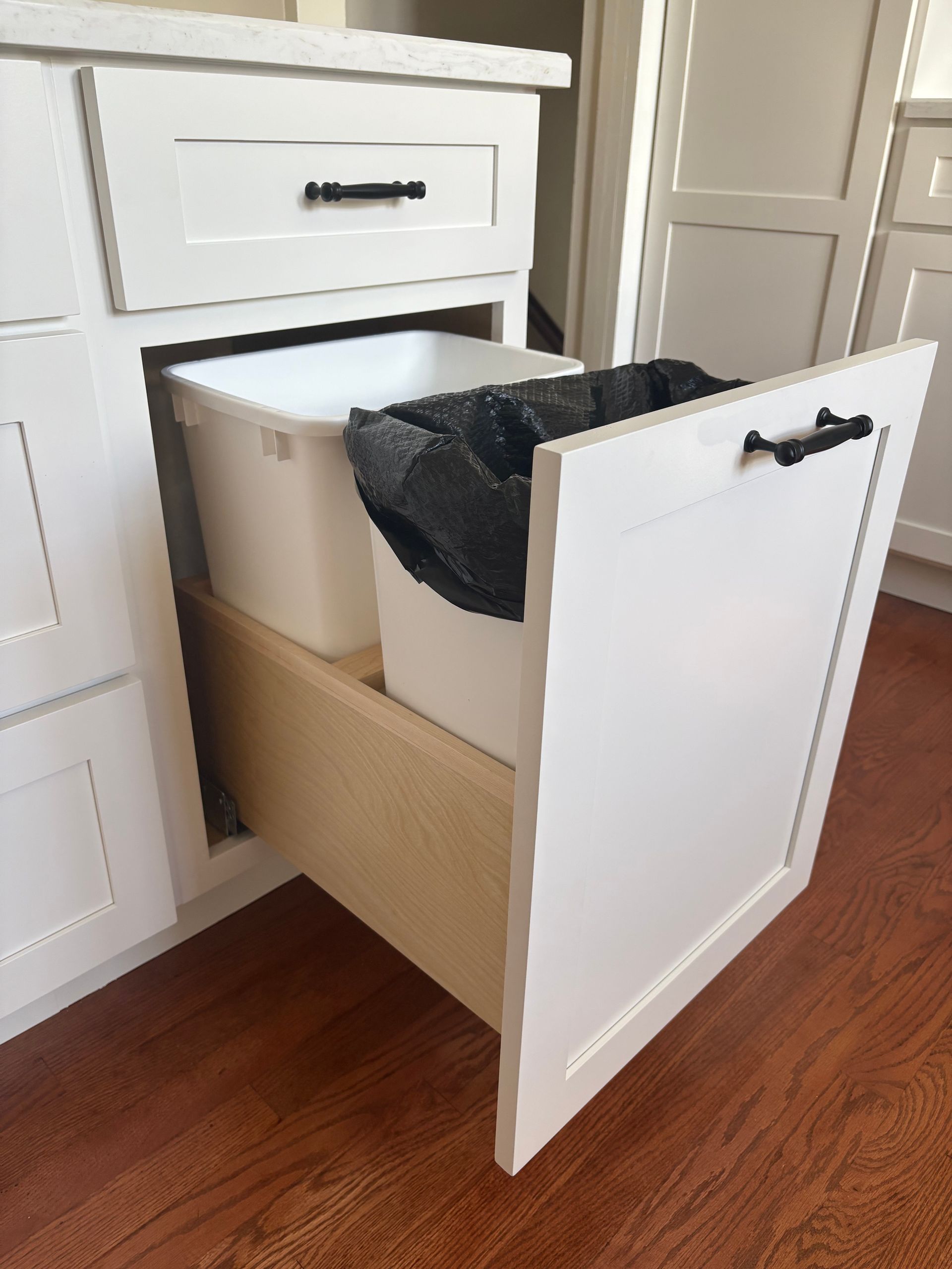 A pull-out cabinet with two trash bins inside. Light beige cabinet with gold hardware.