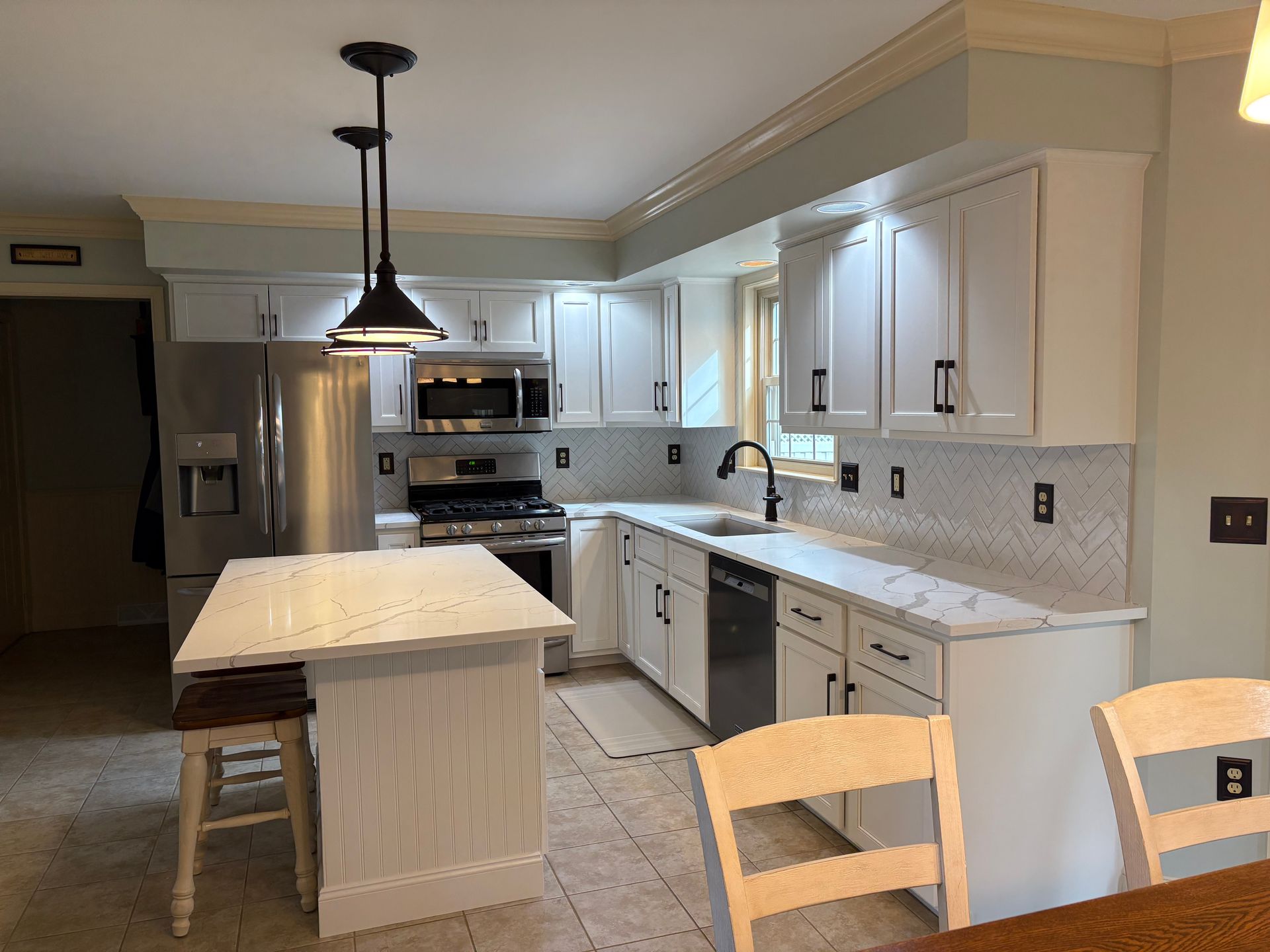 Modern white kitchen with stainless steel appliances, white countertops, and black hardware.