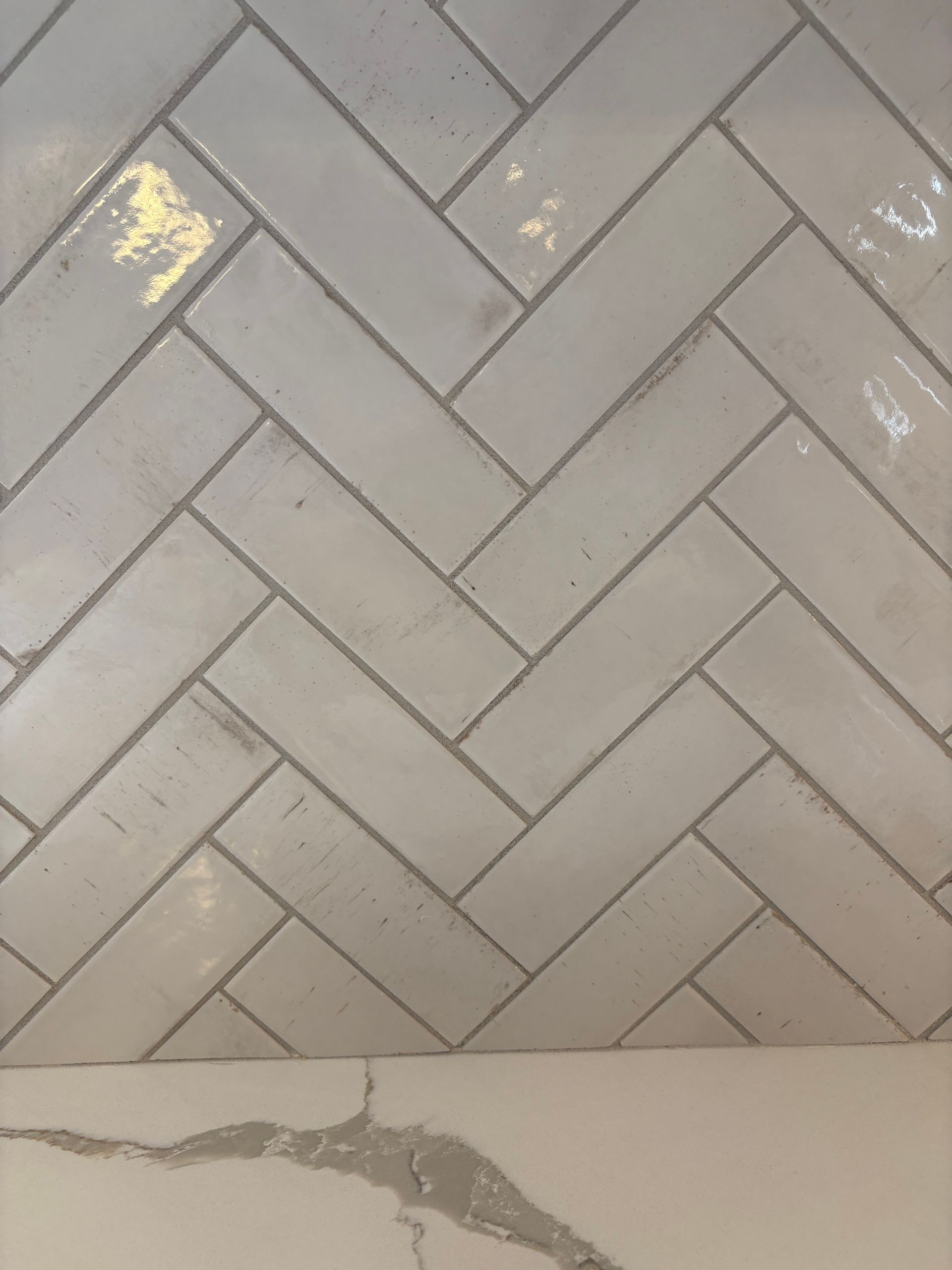 White herringbone tile backsplash above a white countertop with a gray veined pattern.