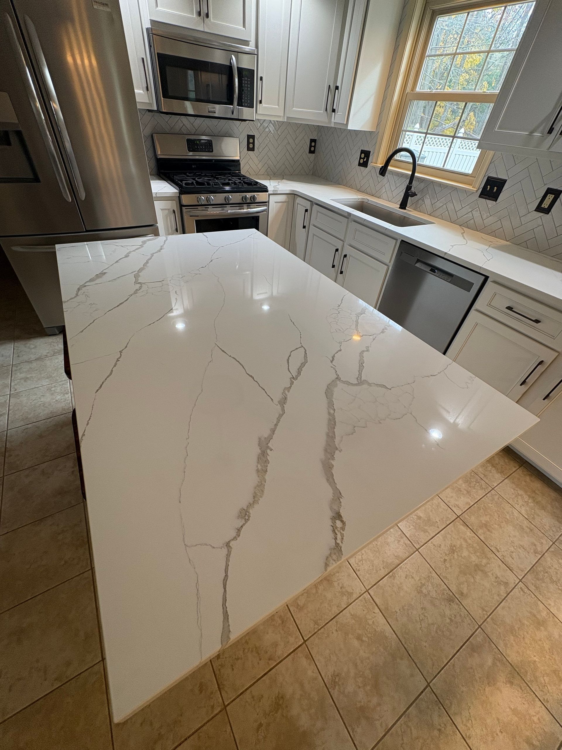 Modern kitchen with white countertops and cabinets, stainless steel appliances, and a marble-look island.