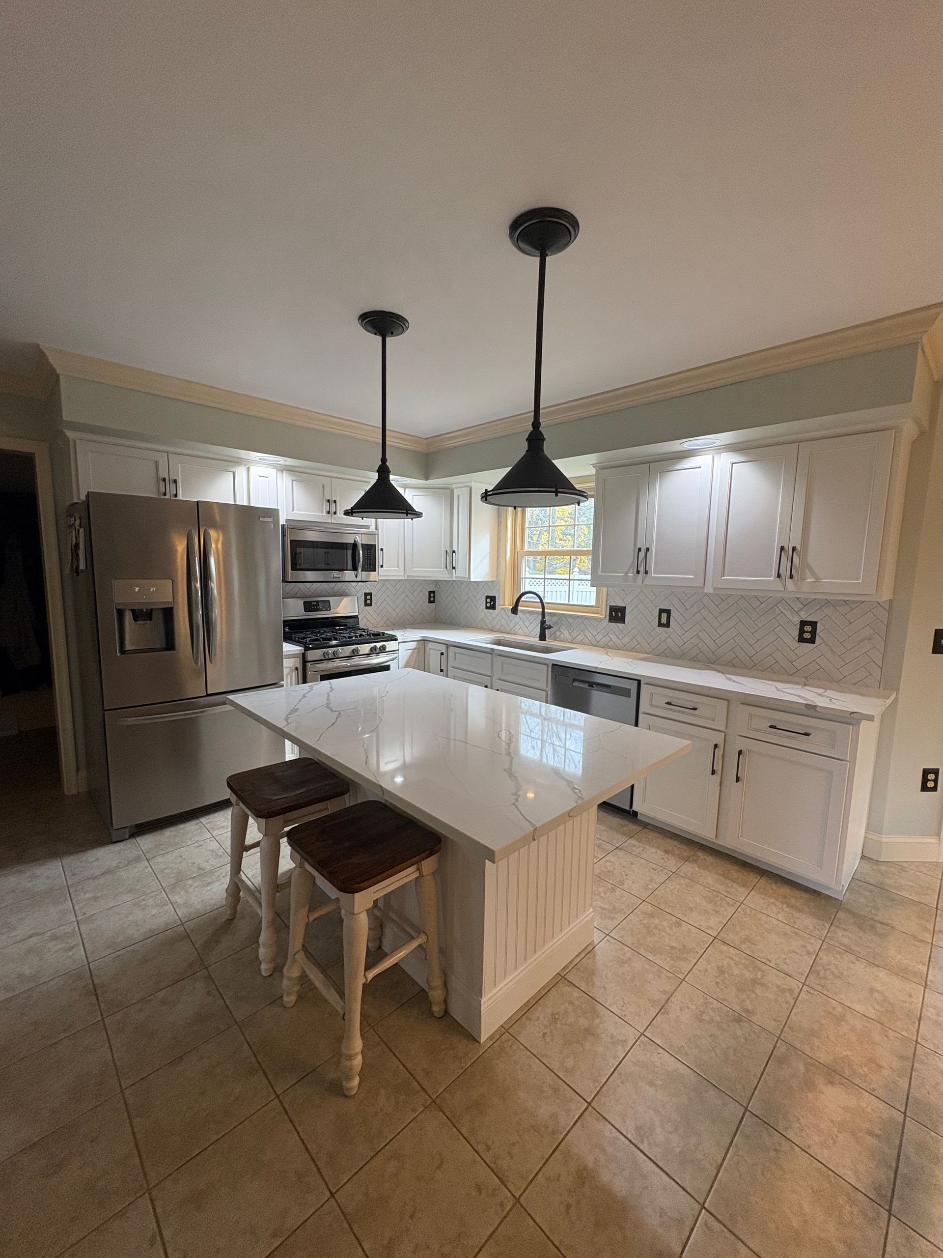 Modern kitchen with white cabinets, island, and pendant lights. Two stools sit at the island.