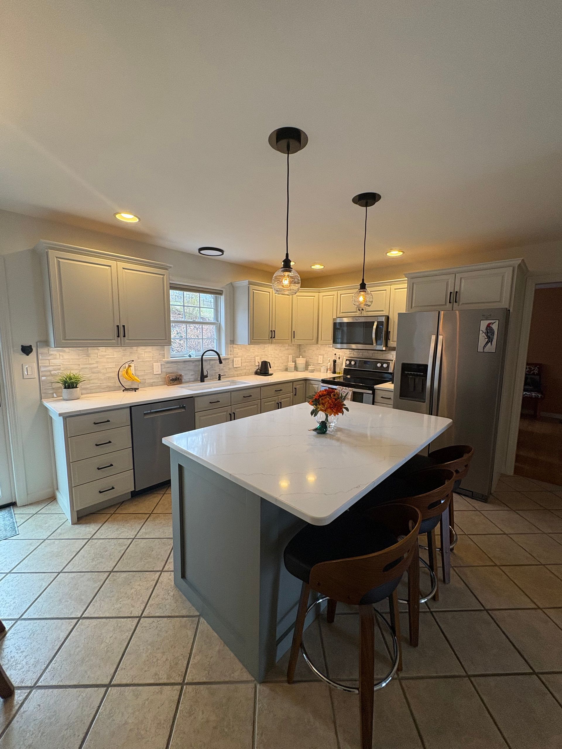 Modern kitchen with gray cabinets, white countertops, island with bar stools, and stainless steel appliances.