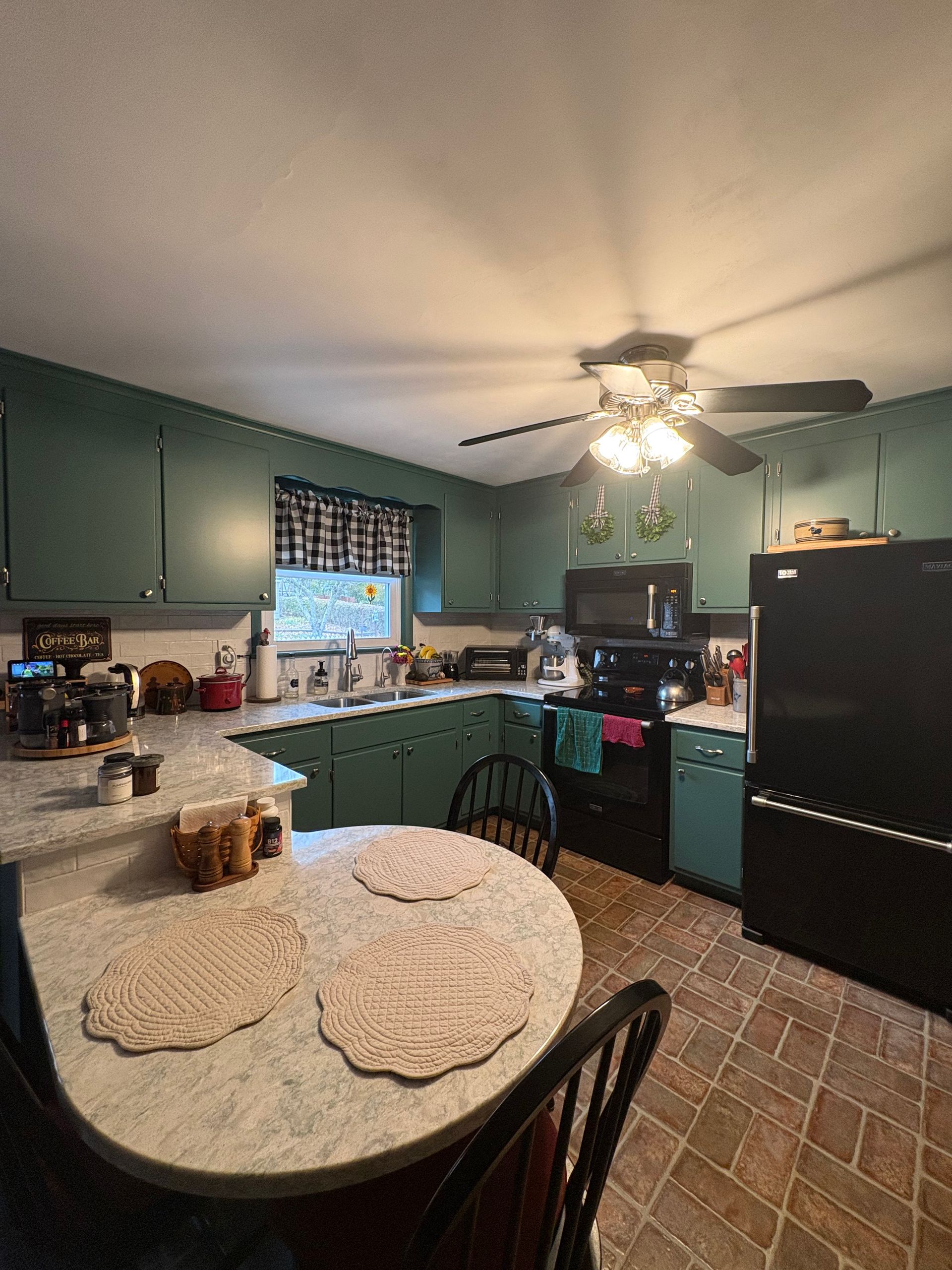 A kitchen with green cabinets, black appliances, and a round table.