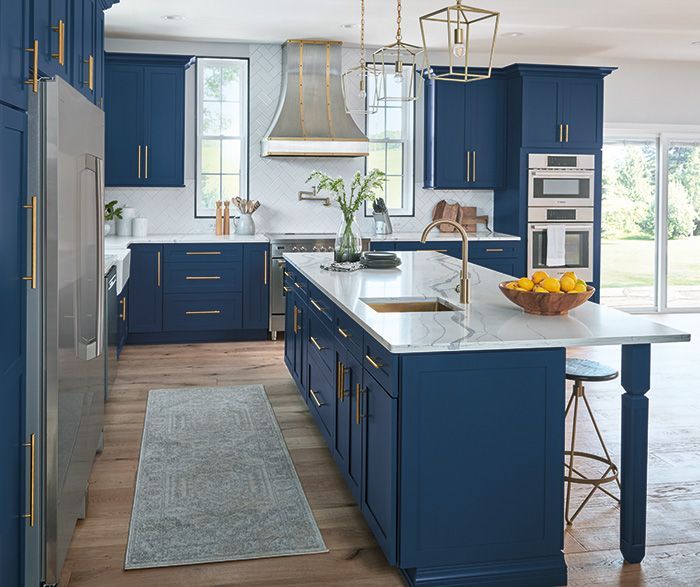 Blue kitchen with white countertops, gold hardware, and a wooden floor.