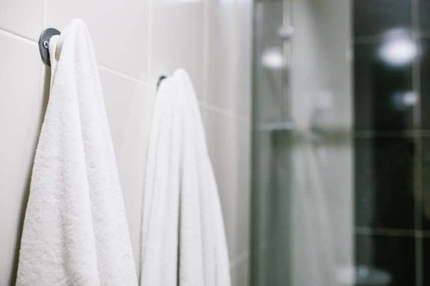 Two white towels hanging on a wall in a bathroom, near a shower.