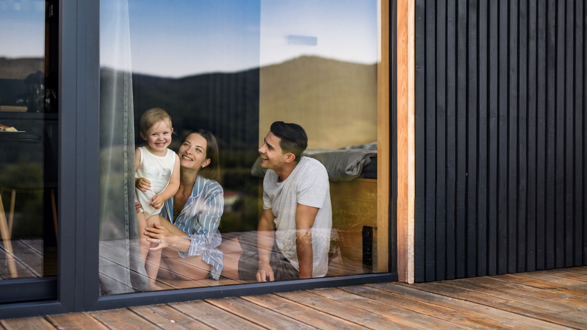 Family smiling inside a modern house, looking out a large window.