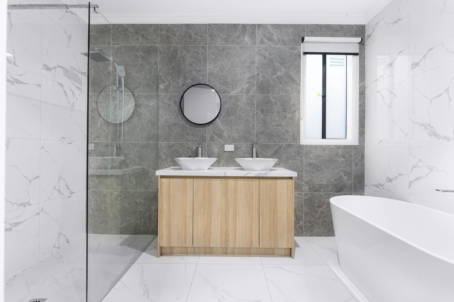 Modern bathroom with double vanity, glass shower, white marble walls, and freestanding tub