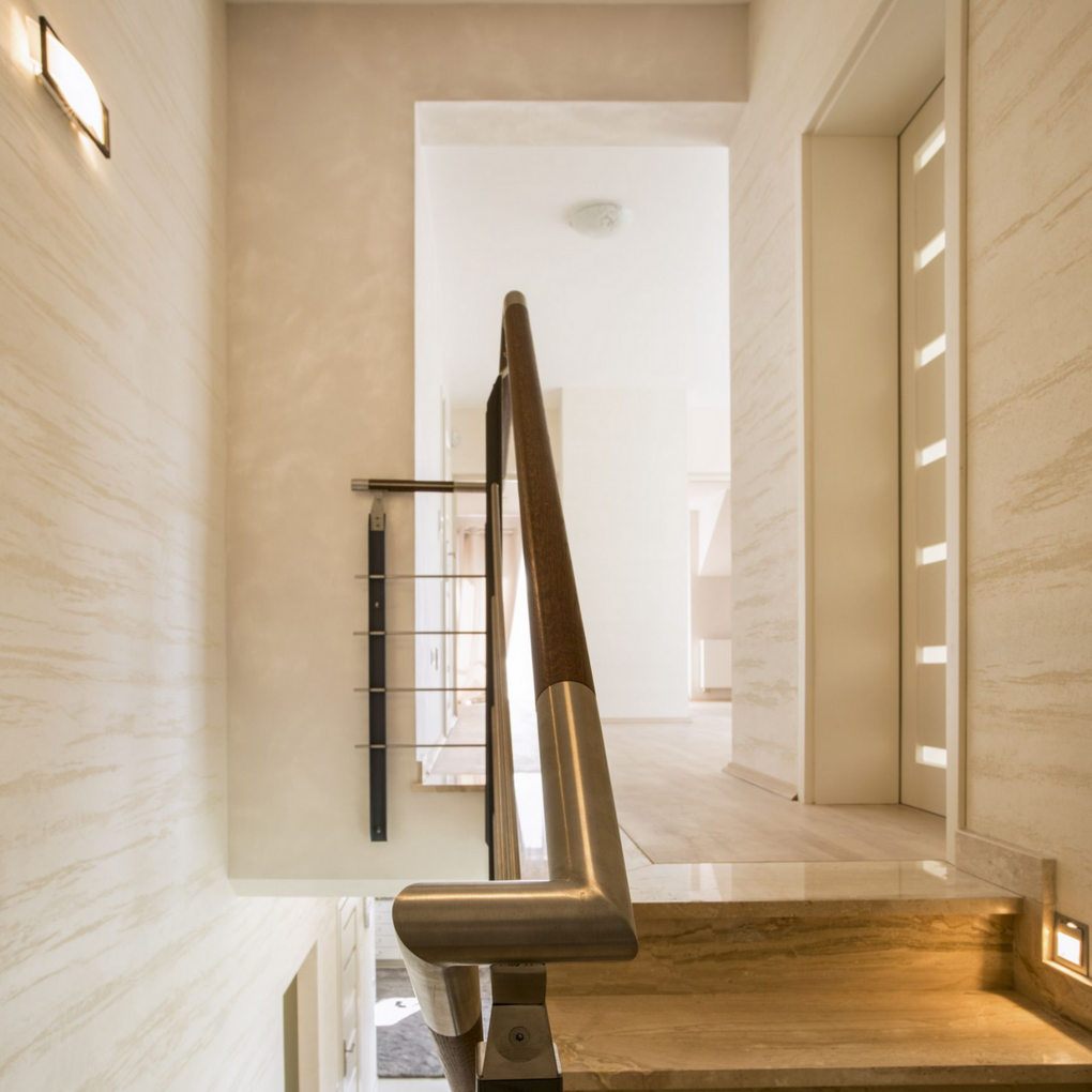 Stairwell with wooden and metal railing, light beige walls, and a view into a hallway.
