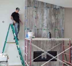 A man is standing on a ladder in front of a fireplace.