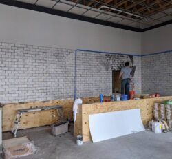 A man is painting a white brick wall in a room.