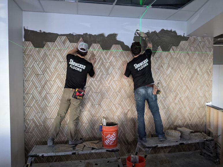 Two men are working on a wall with a home depot bucket in the foreground.