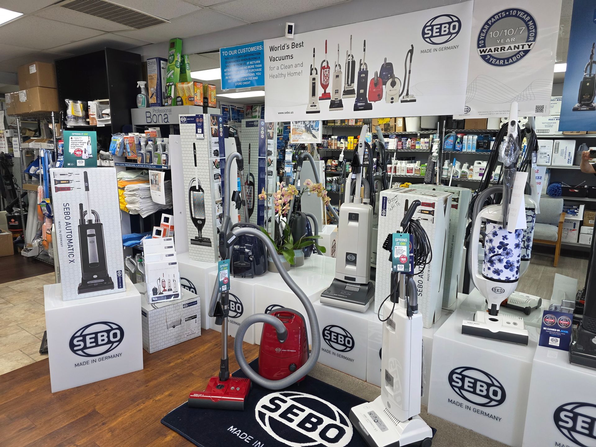 A showroom display of various SEBO vacuum cleaners, featuring several upright and canister models on white pedestals.