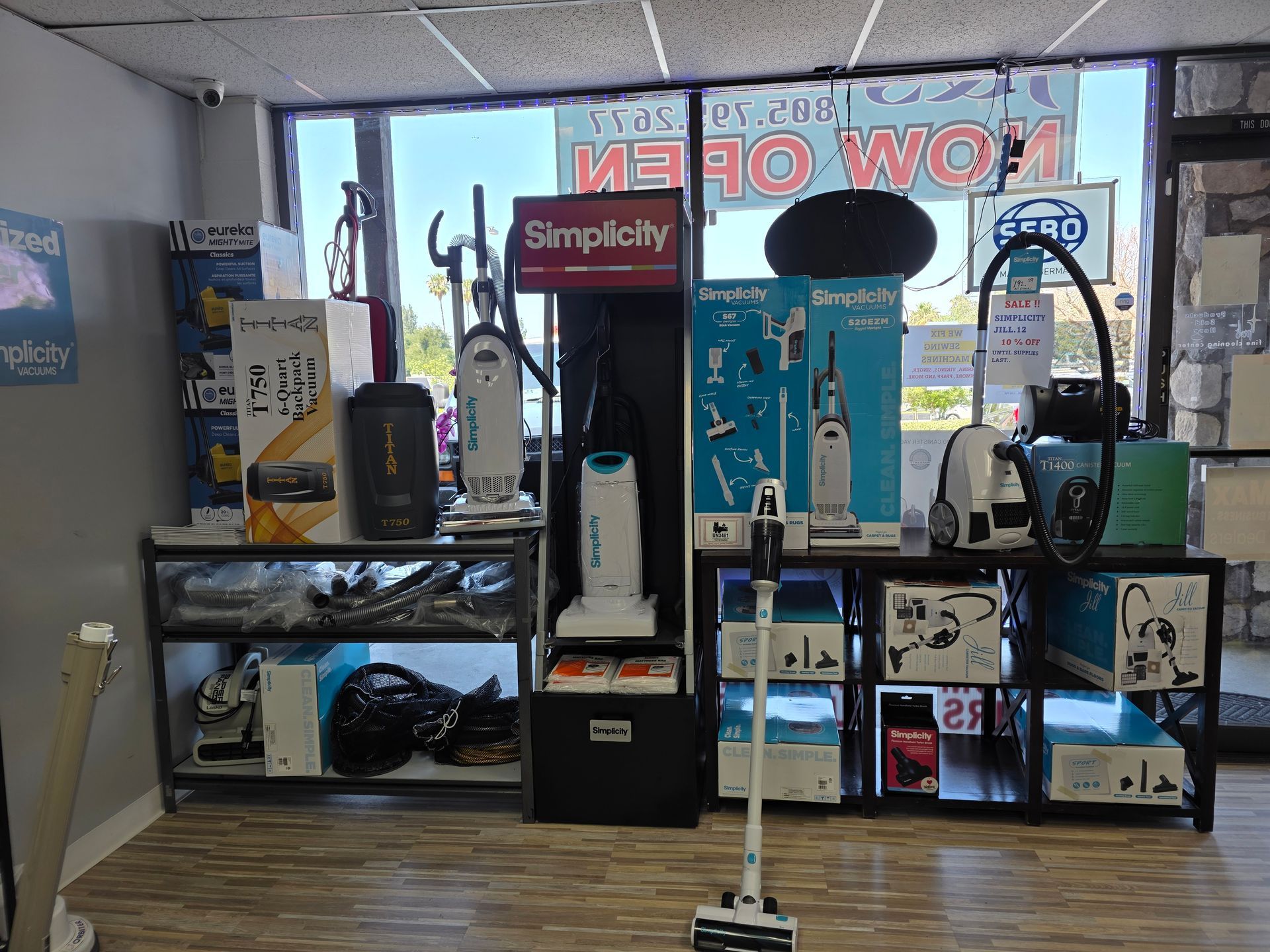 A retail store display featuring various vacuum cleaners and boxes, positioned on shelves and the floor in front of a window.