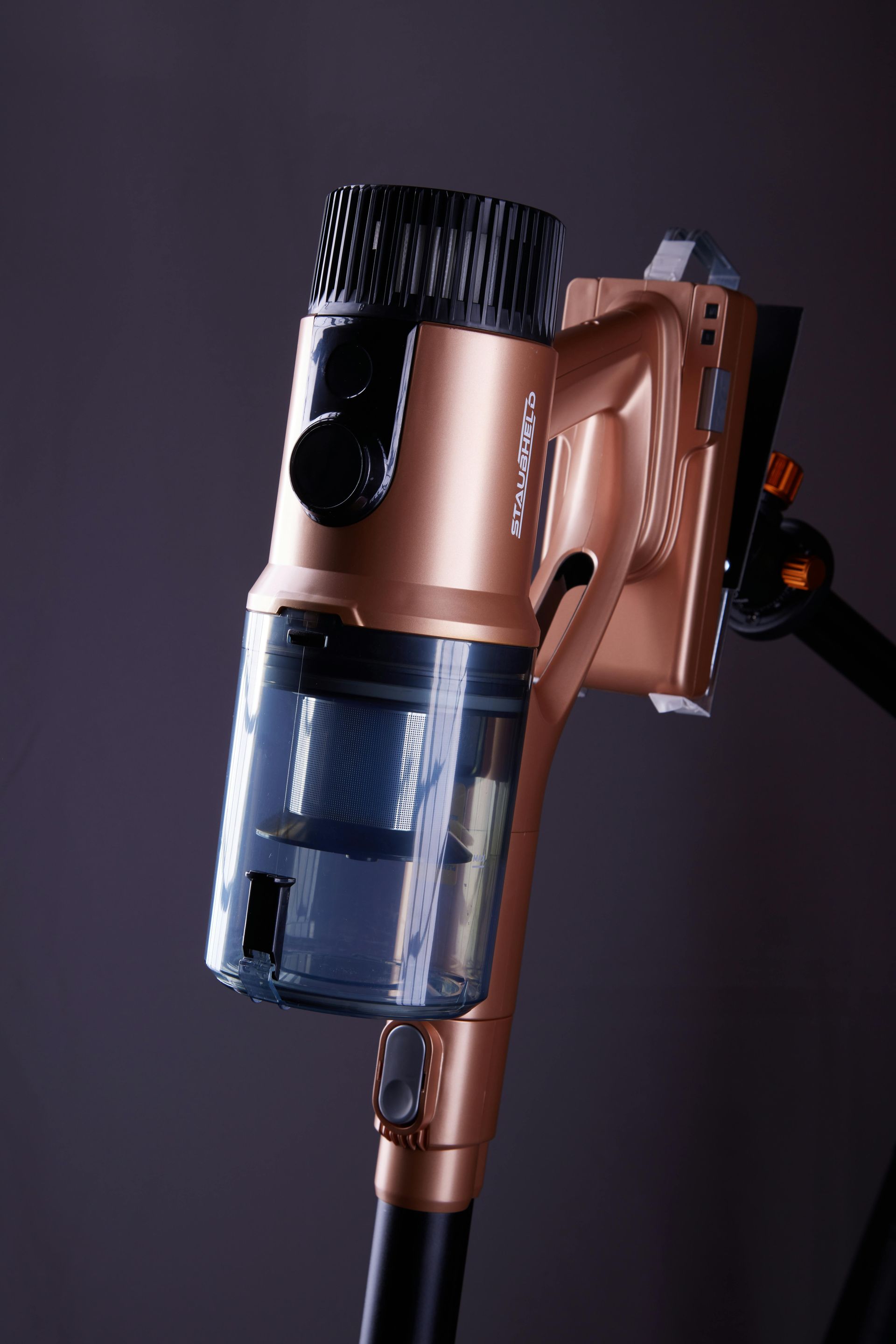 A blue canister vacuum cleaner sits on a light-colored floor against a plain gray wall.