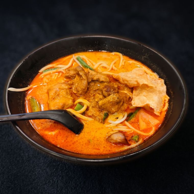 Red noodle soup with beef, scallions, and crispy crackers in a black bowl with a spoon