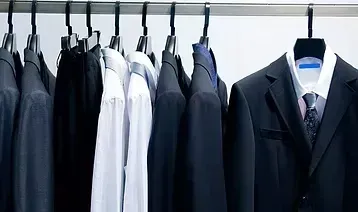 Un perchero exhibe varios trajes oscuros y camisas blancas de vestir en perchas negras.