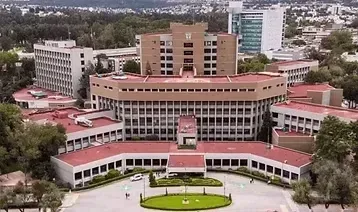 Vista aérea de un gran complejo de edificios gubernamentales de varias plantas con tejados rojos, rodeado de árboles y vegetación.