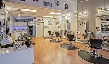 Una peluquería moderna y luminosa con cuatro sillones de peluquería sobre colchonetas circulares, un mostrador de recepción y expositores de productos.