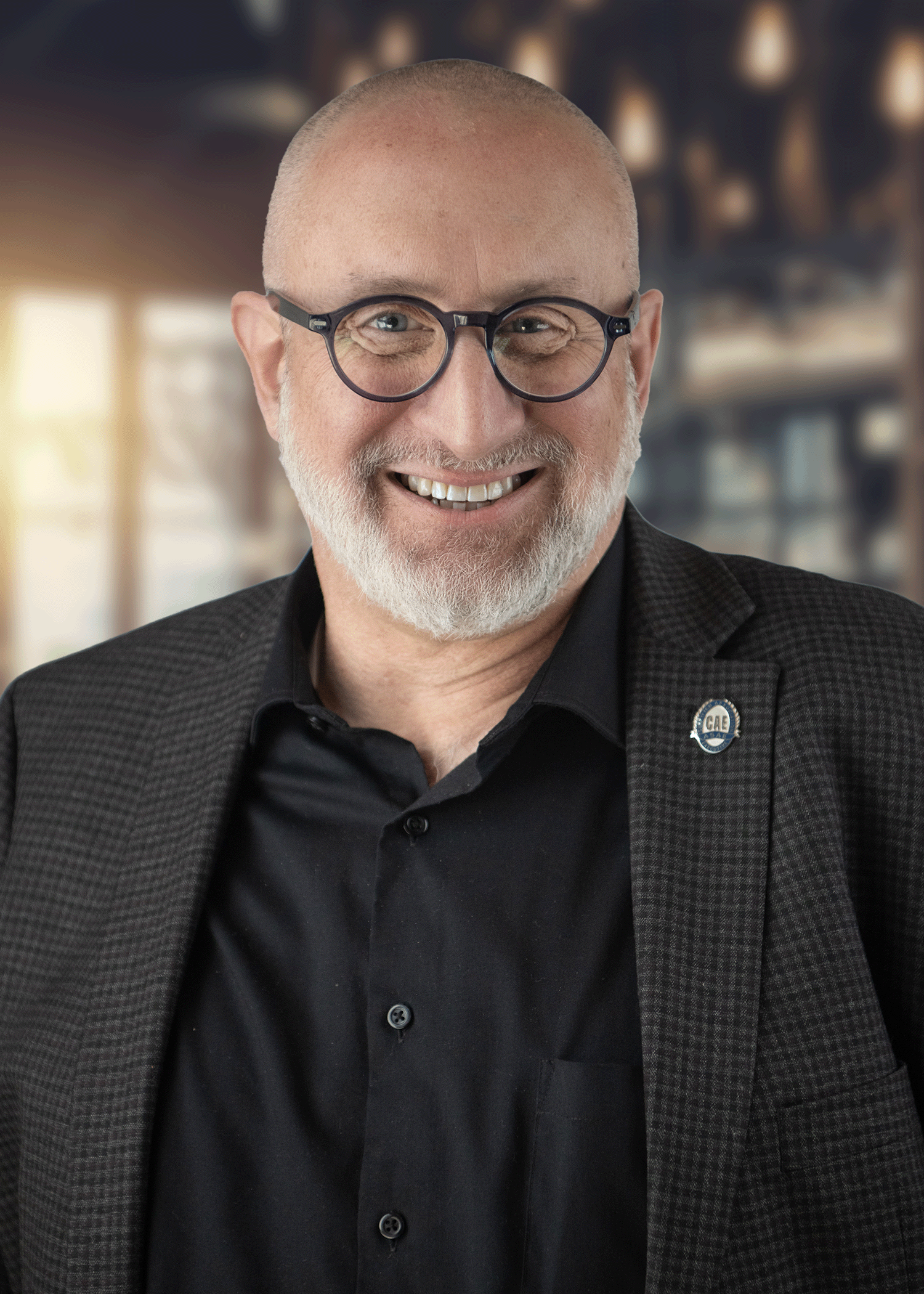 Man in blue shirt and blazer smiles by a wooden fence.