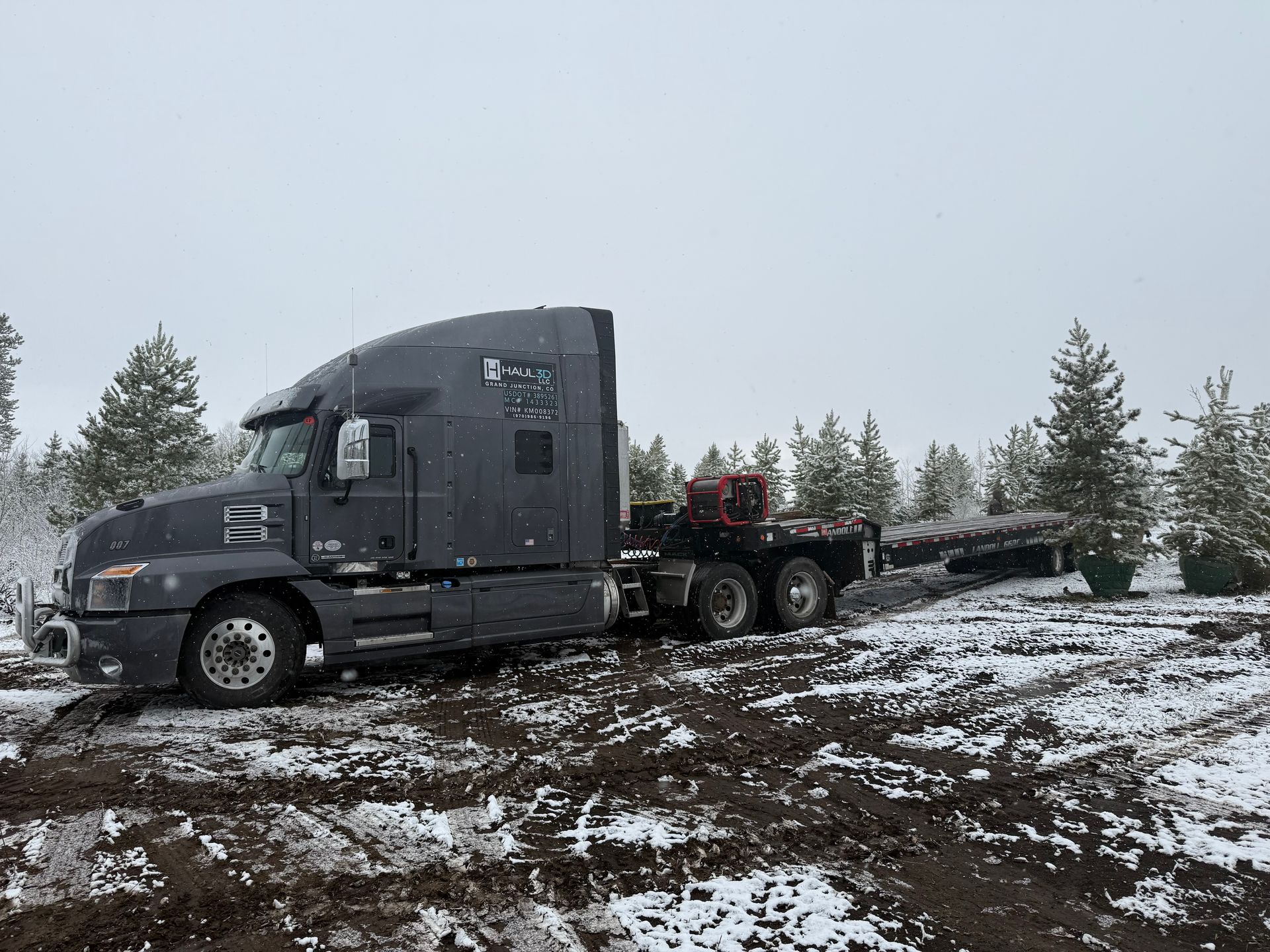 orange construction equipment on flatbed gooseneck trailer being hauled by haul3d across colorado mountains