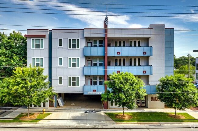 Modern apartment building exterior with blue accents, balconies, and small trees.