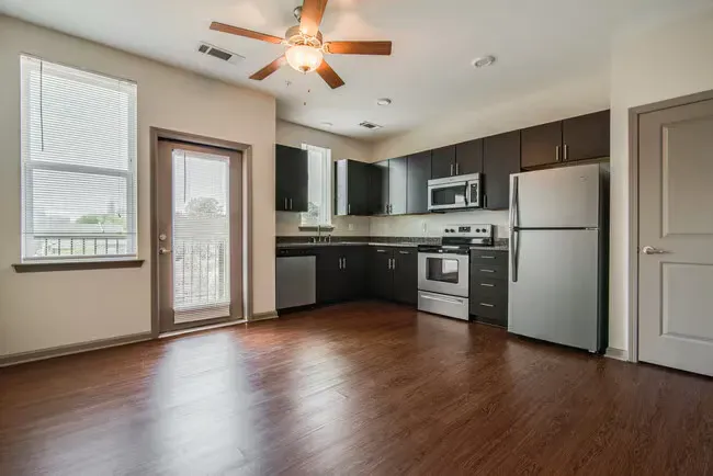 Modern apartment kitchen with dark cabinetry, stainless steel appliances, and wood floors.