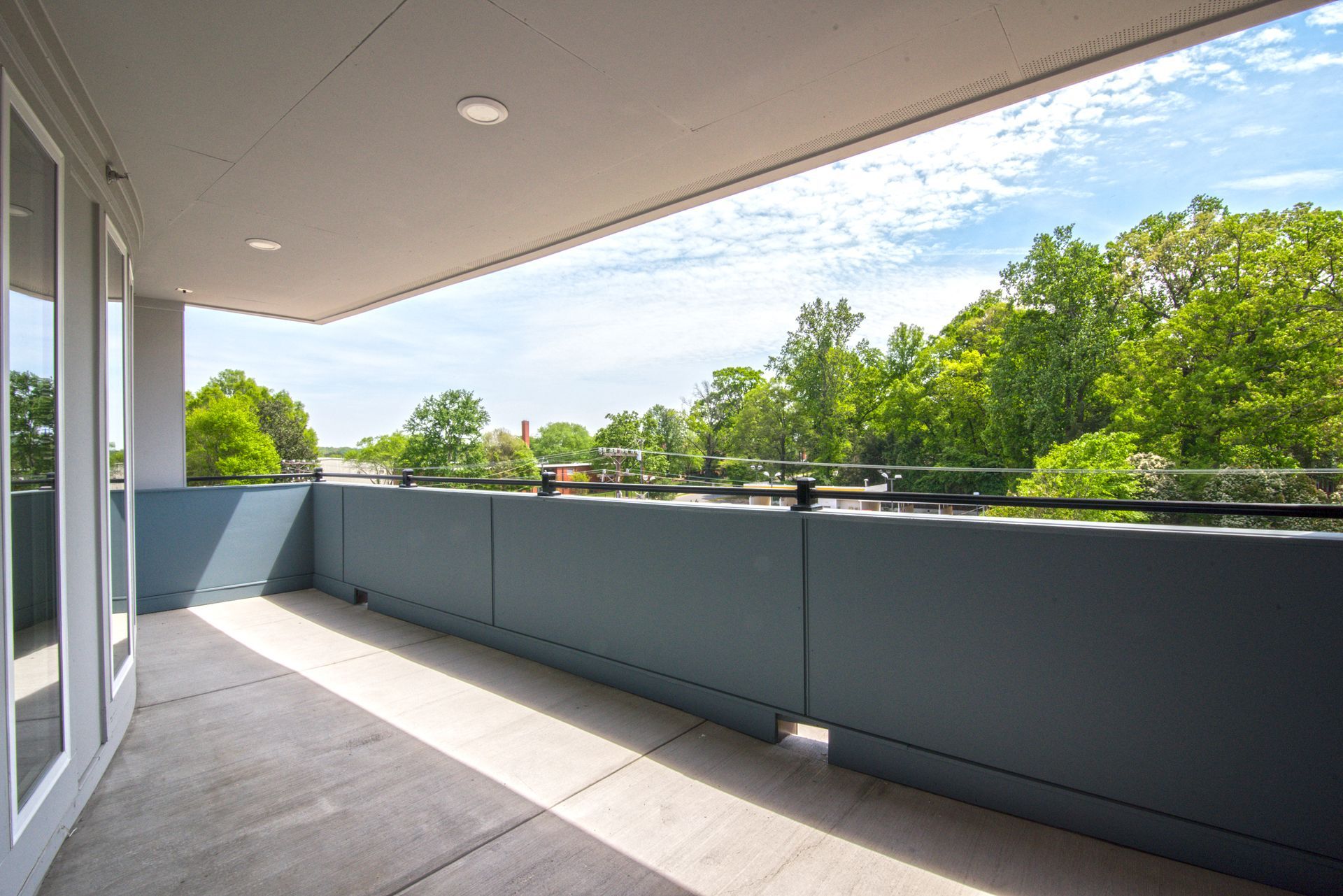 Balcony with gray walls, concrete floor, and green trees in the background under a blue sky.