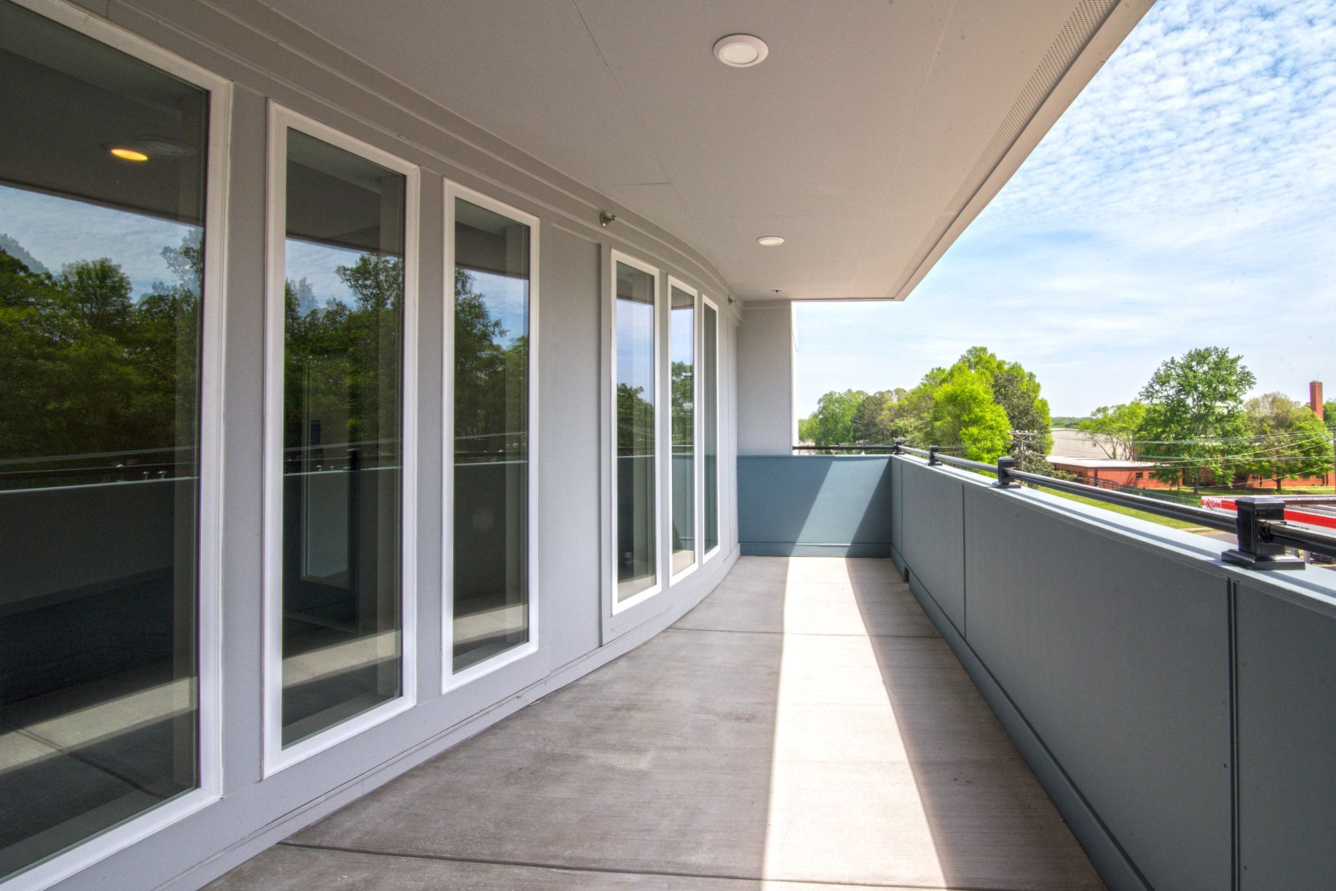 Balcony with gray floor and railing, glass doors, and blue sky.