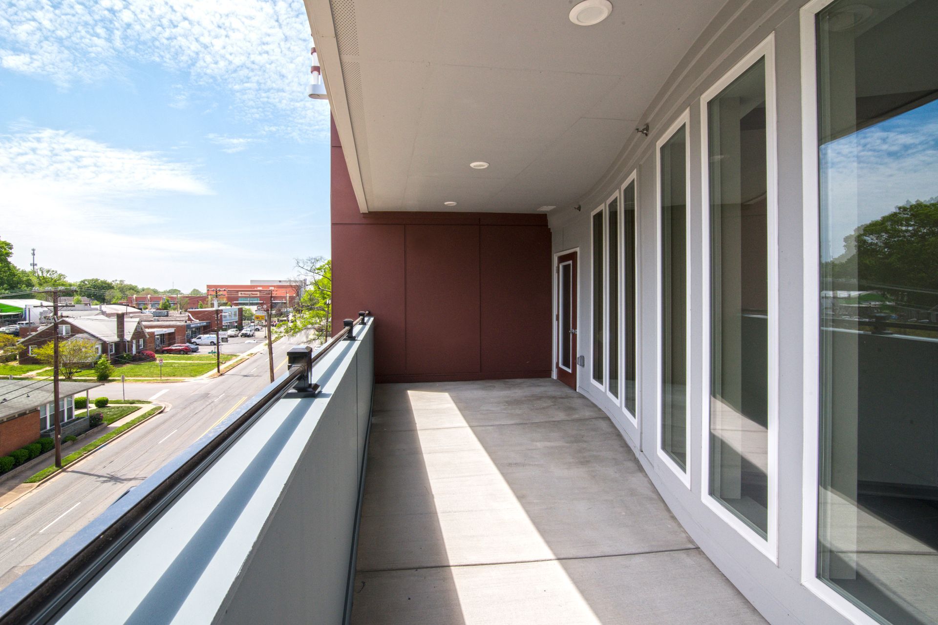 Balcony overlooking a street, with glass doors, gray walls, and blue sky.