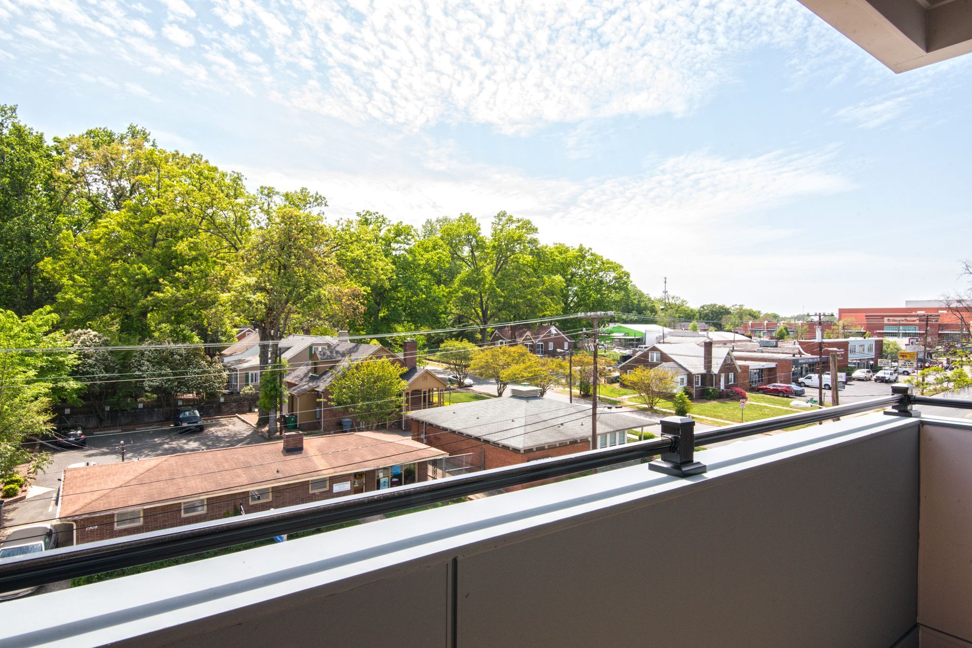 View from a balcony overlooking a street lined with houses, trees, and a cloudy blue sky.