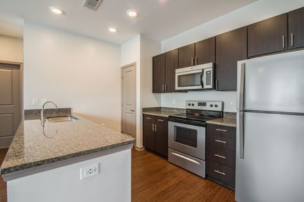 Modern kitchen with granite counters, stainless steel appliances, dark cabinets, and wood floors.
