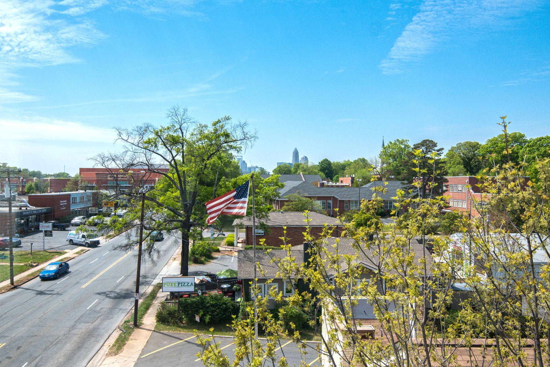 City street view with cars, businesses, and the American flag under a blue sky.
