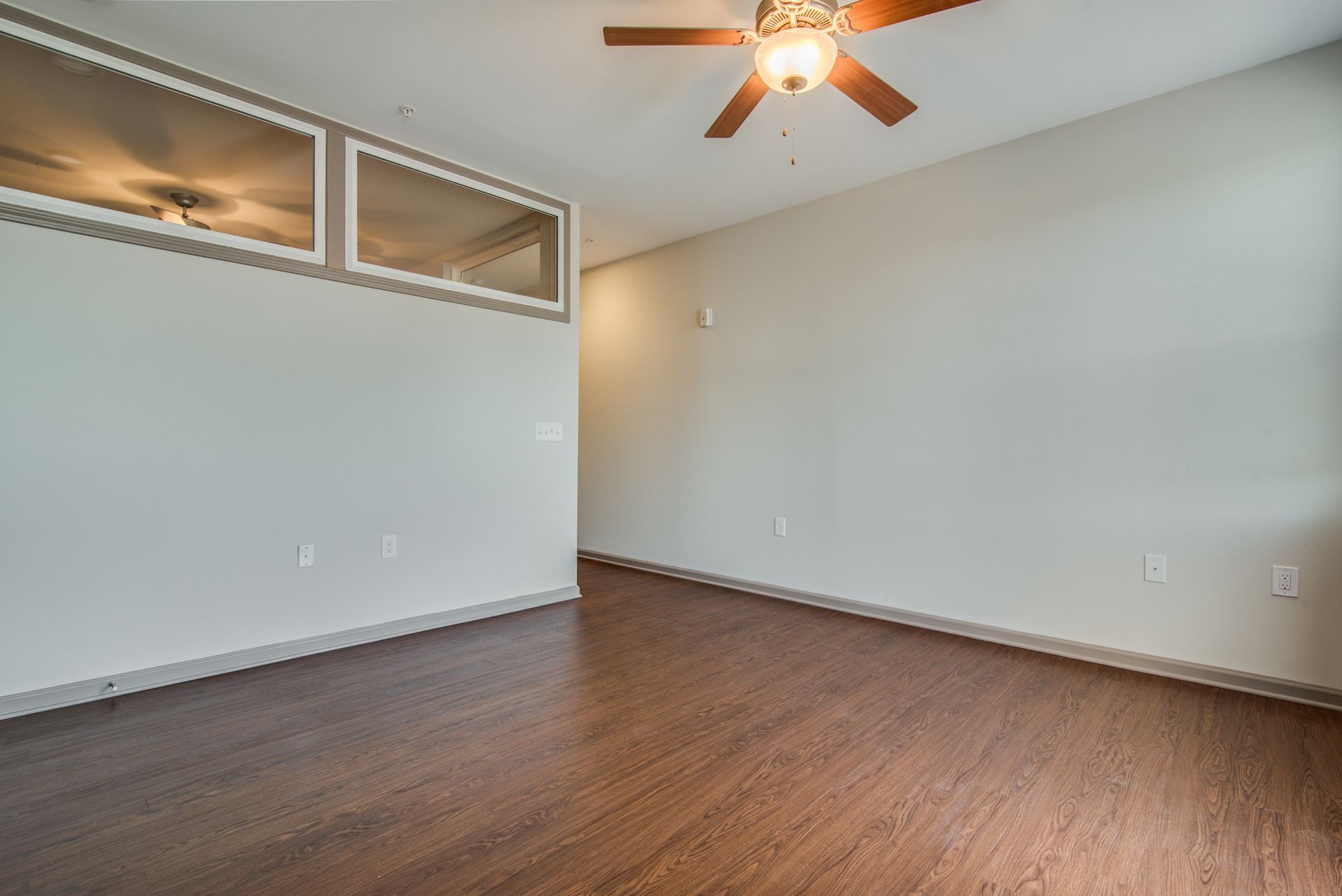 Empty room with wood flooring, pale walls, and a ceiling fan.