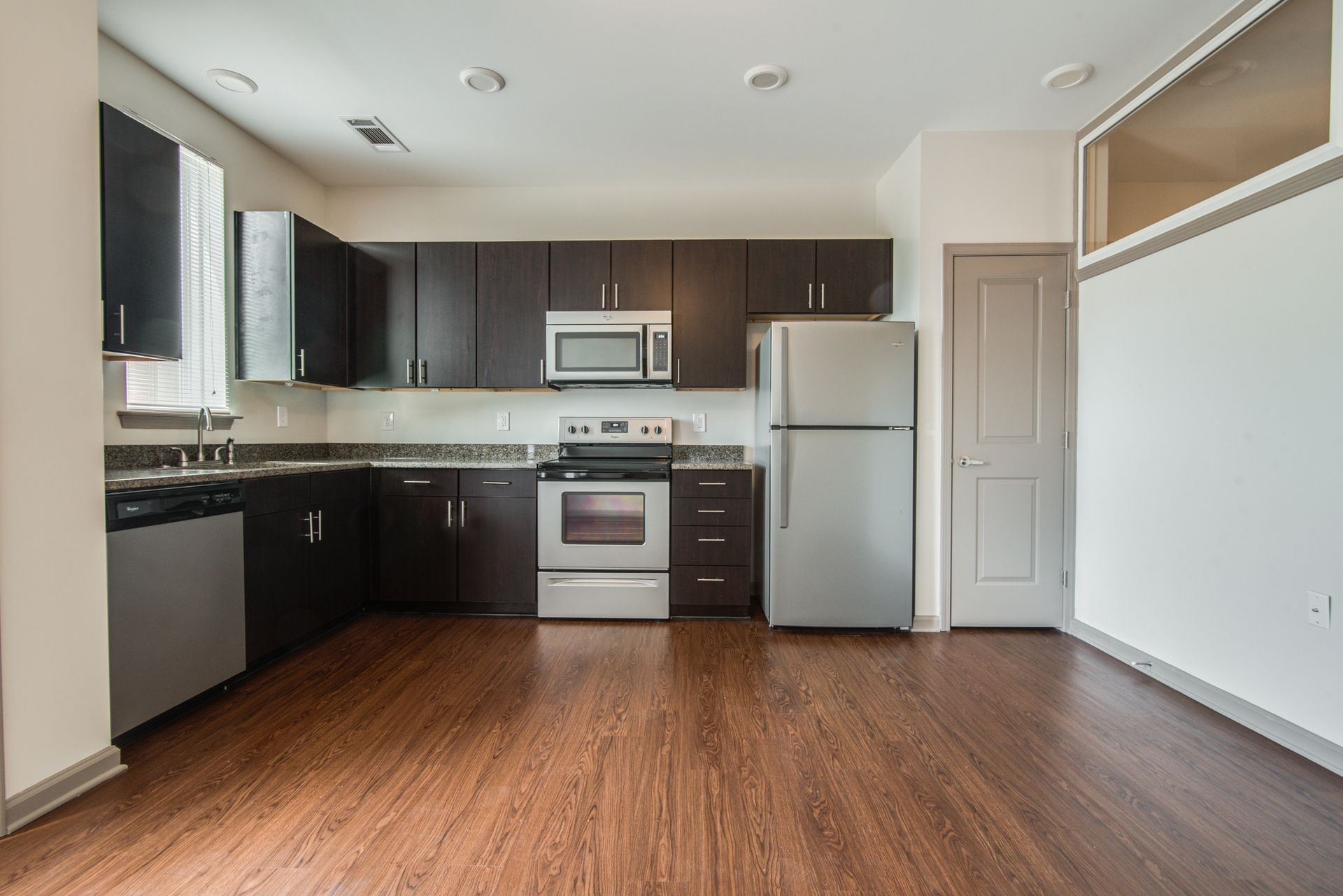 Modern kitchen with dark cabinets, stainless steel appliances, and wood flooring.