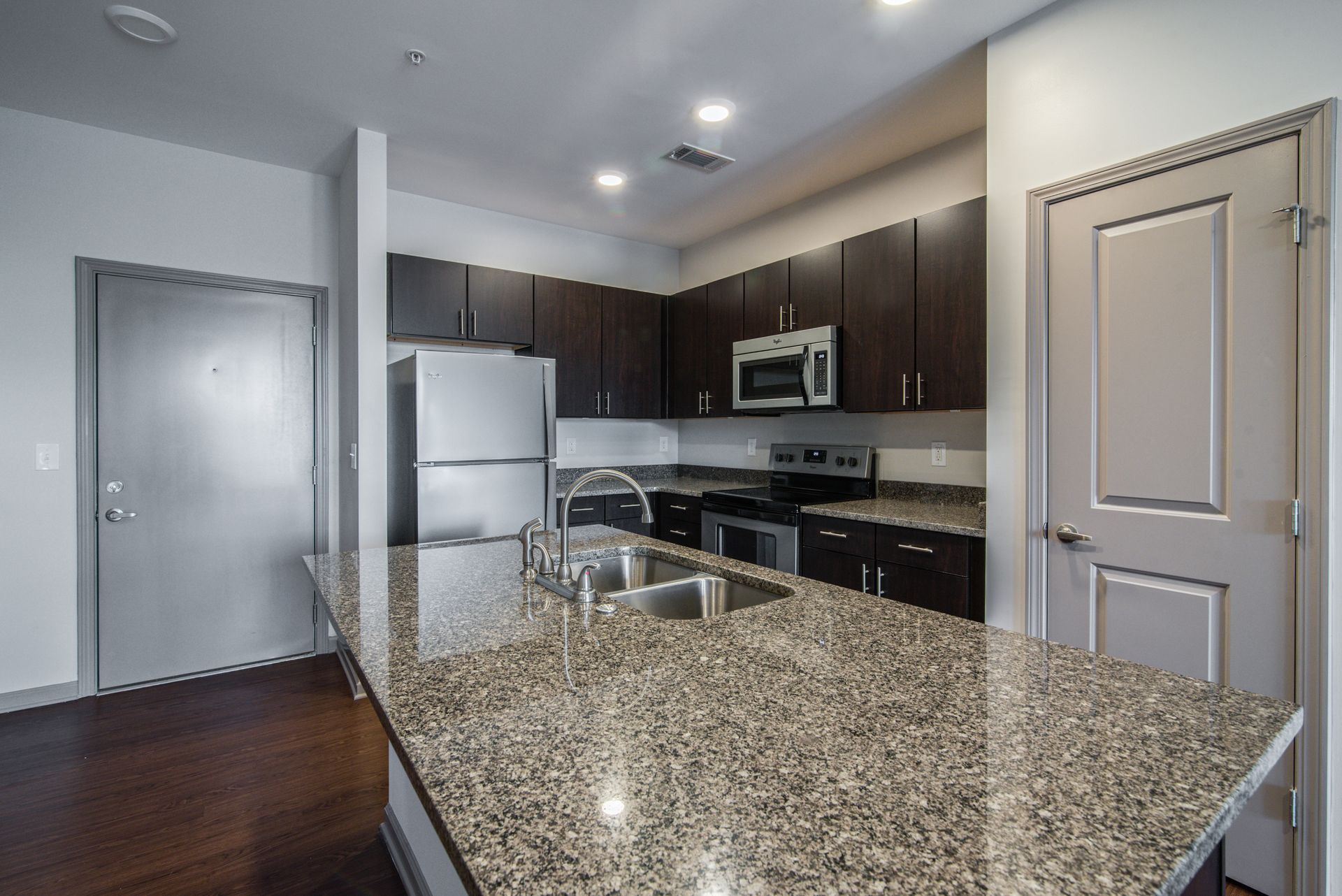 Kitchen with granite countertops, dark cabinets, stainless steel appliances, and a wooden floor.