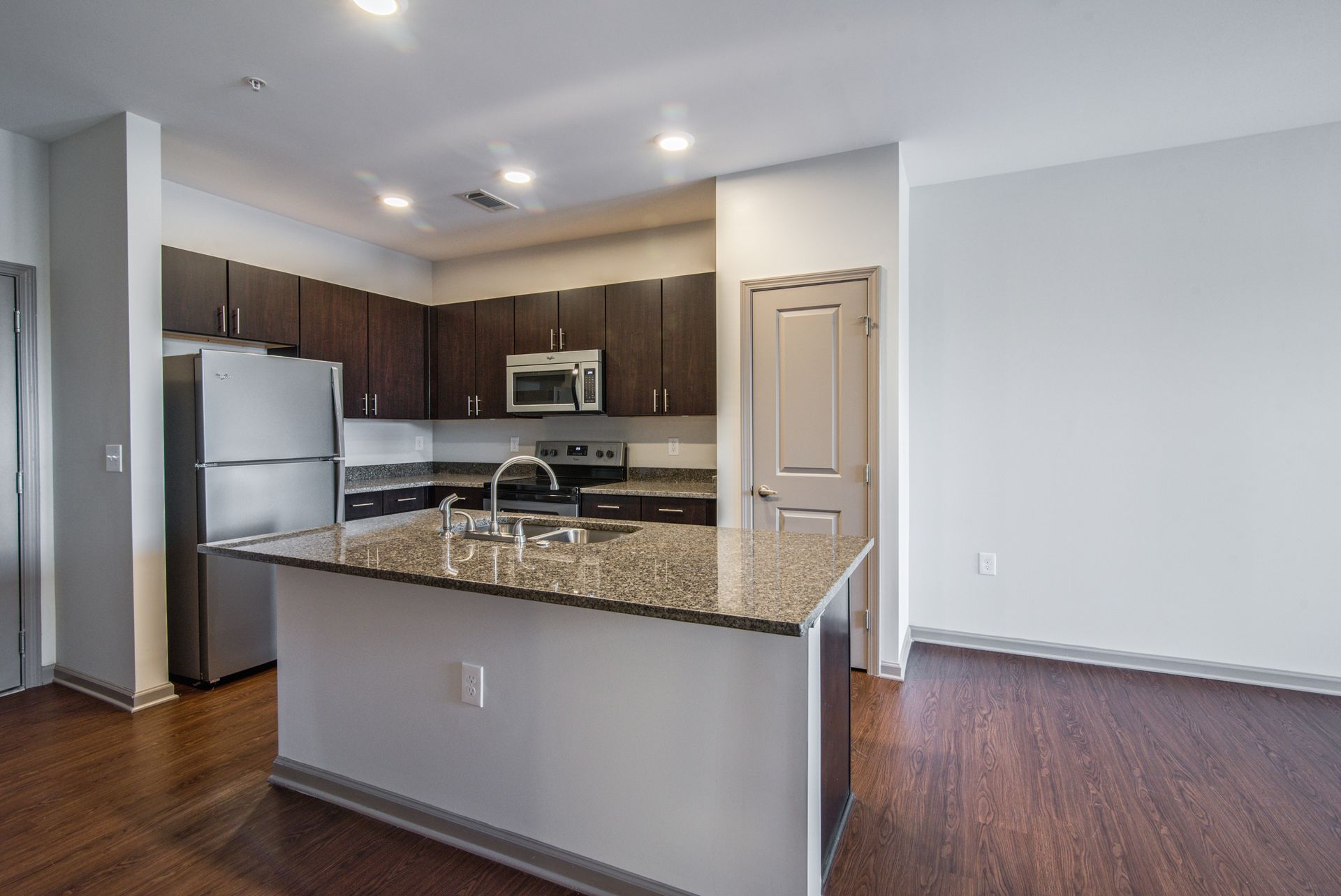 Modern kitchen with dark wood cabinets, stainless steel appliances, granite island, and hardwood floors.