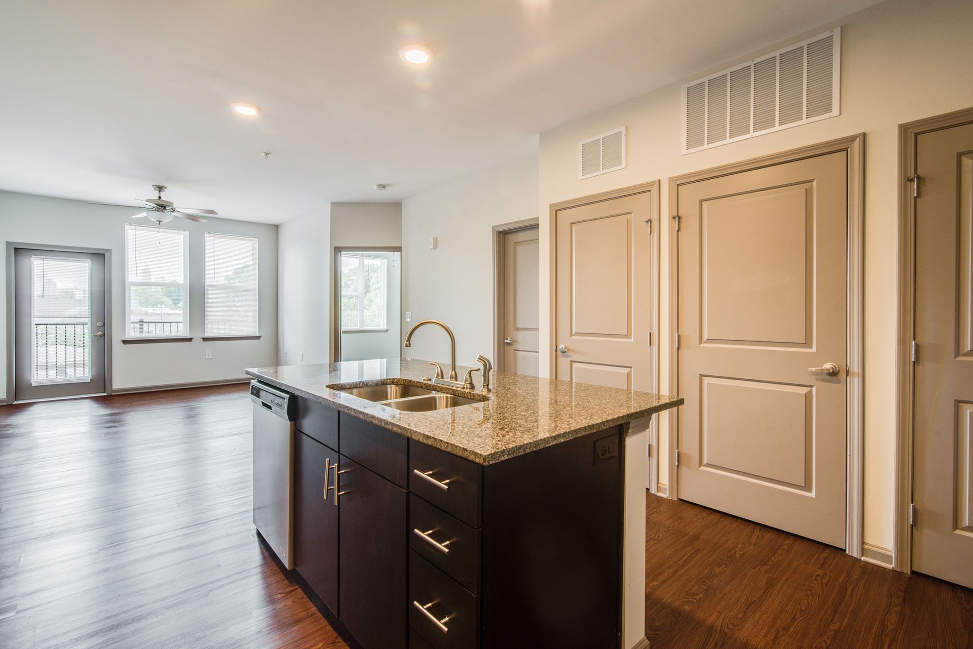 Open-concept kitchen and living room with hardwood floors, granite island, and doors to a balcony.
