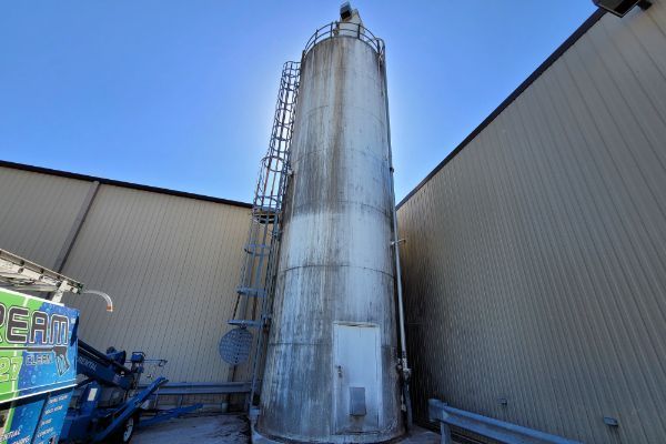 A large stainless steel silo is sitting outside of a building.