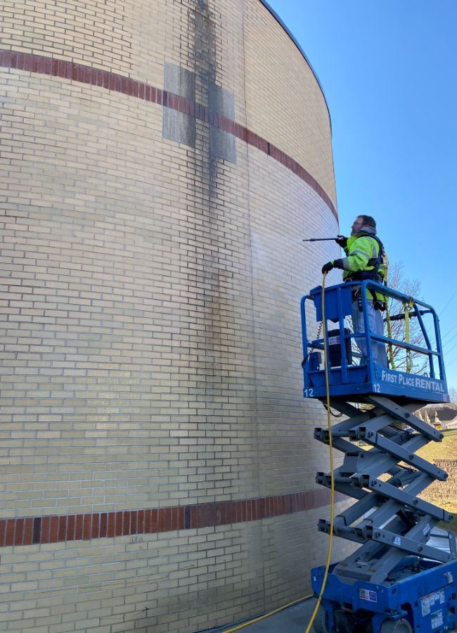 A man is standing on a scissor lift cleaning a brick wall.