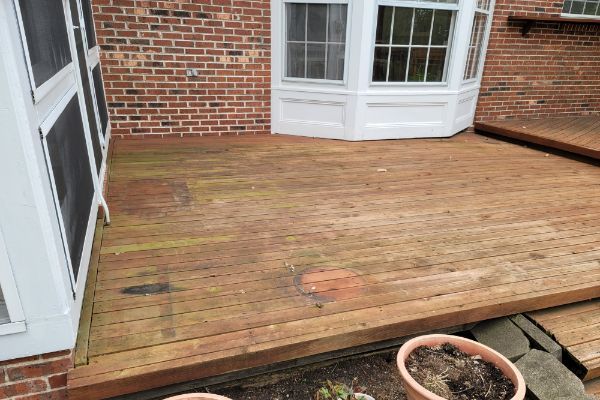 A wooden deck with potted plants on it in front of a brick house.