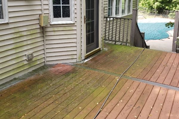 A wooden deck with moss growing on it in front of a house.
