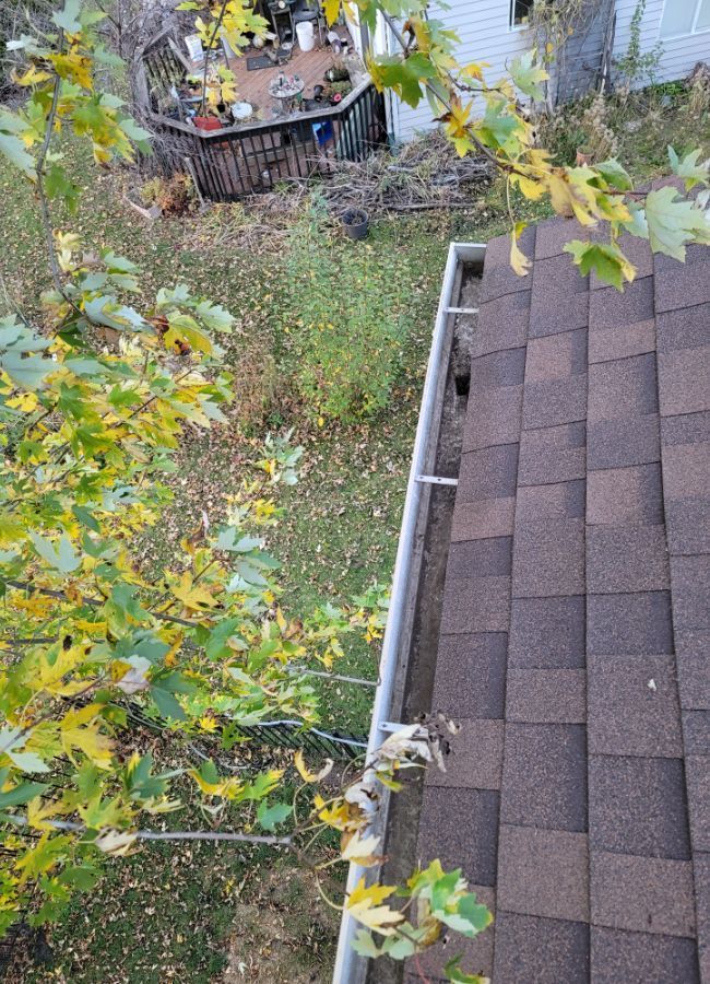 A roof with a gutter on it and a deck in the background.