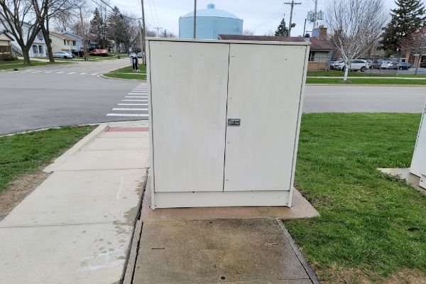 A white cabinet is sitting on a sidewalk next to a street.