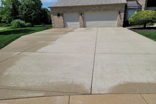 A concrete driveway leading to a house with two garage doors.
