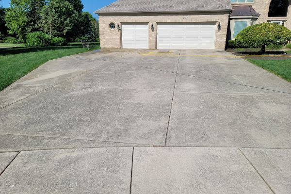 A concrete driveway leading to a house with two garage doors.