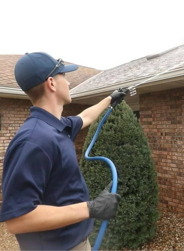A man in a blue shirt is spraying a roof with a hose