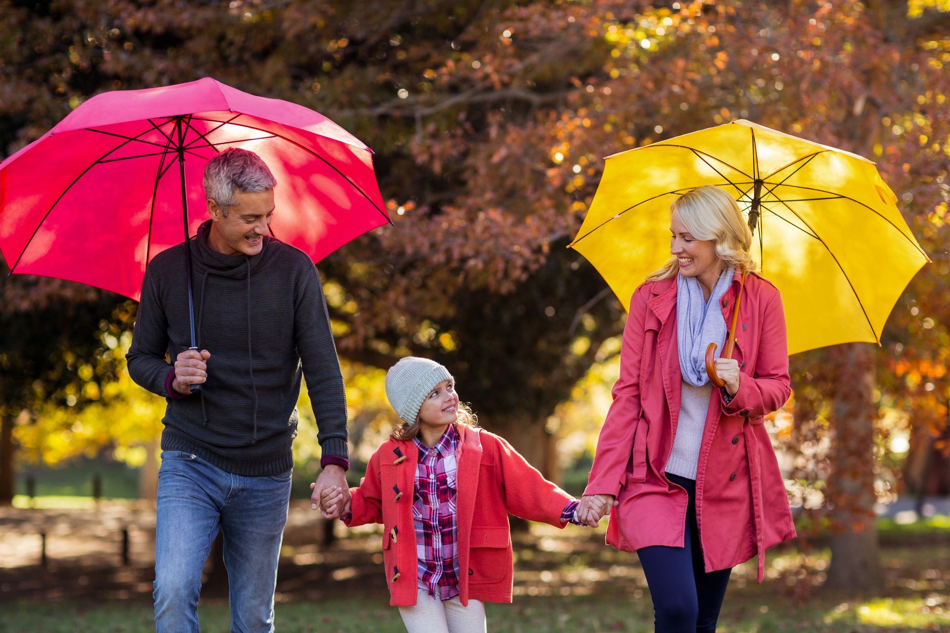 Three people walking in a park with red and yellow umbrellas in autumn