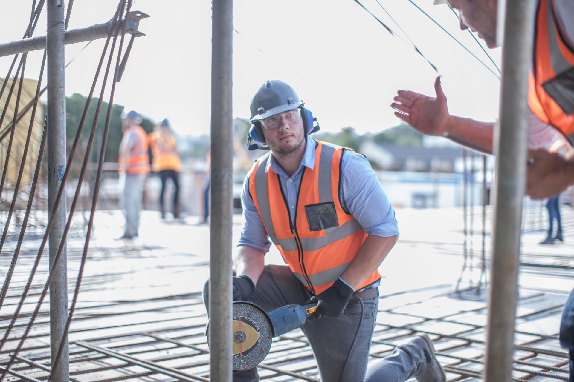 Construction worker in orange vest and blue hard hat cutting rebar on a building site