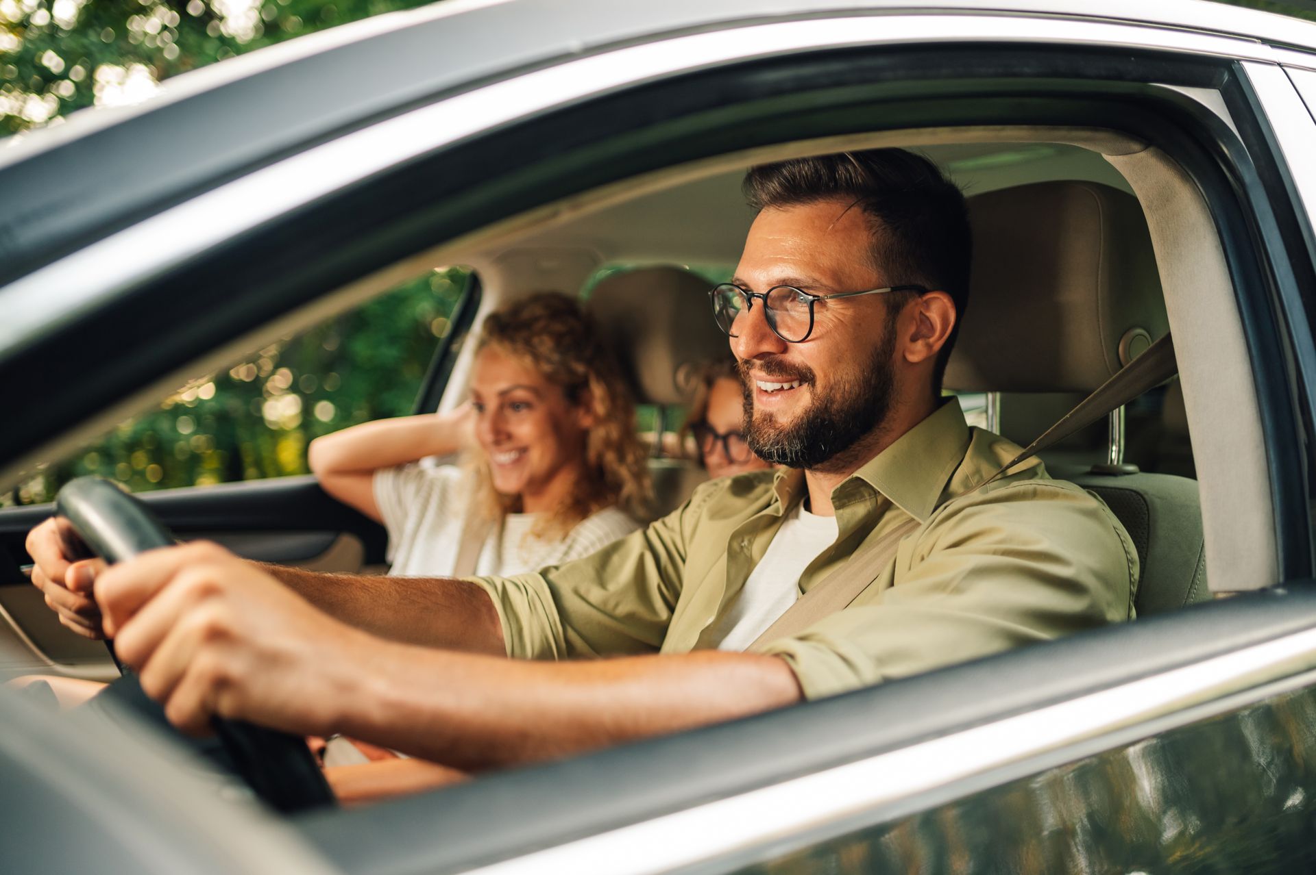 Two people smiling in a car, with the driver holding the steering wheel